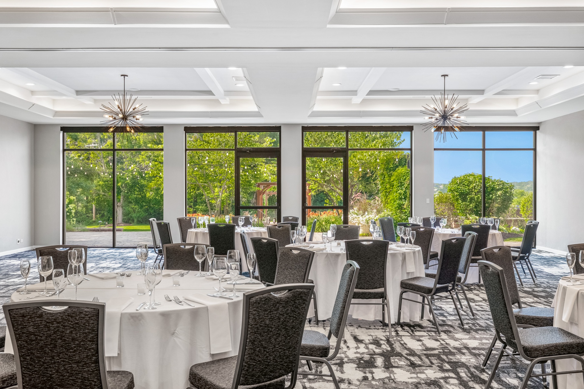 Elegant ballroom set with round tables and garden views through floor-to-ceiling windows