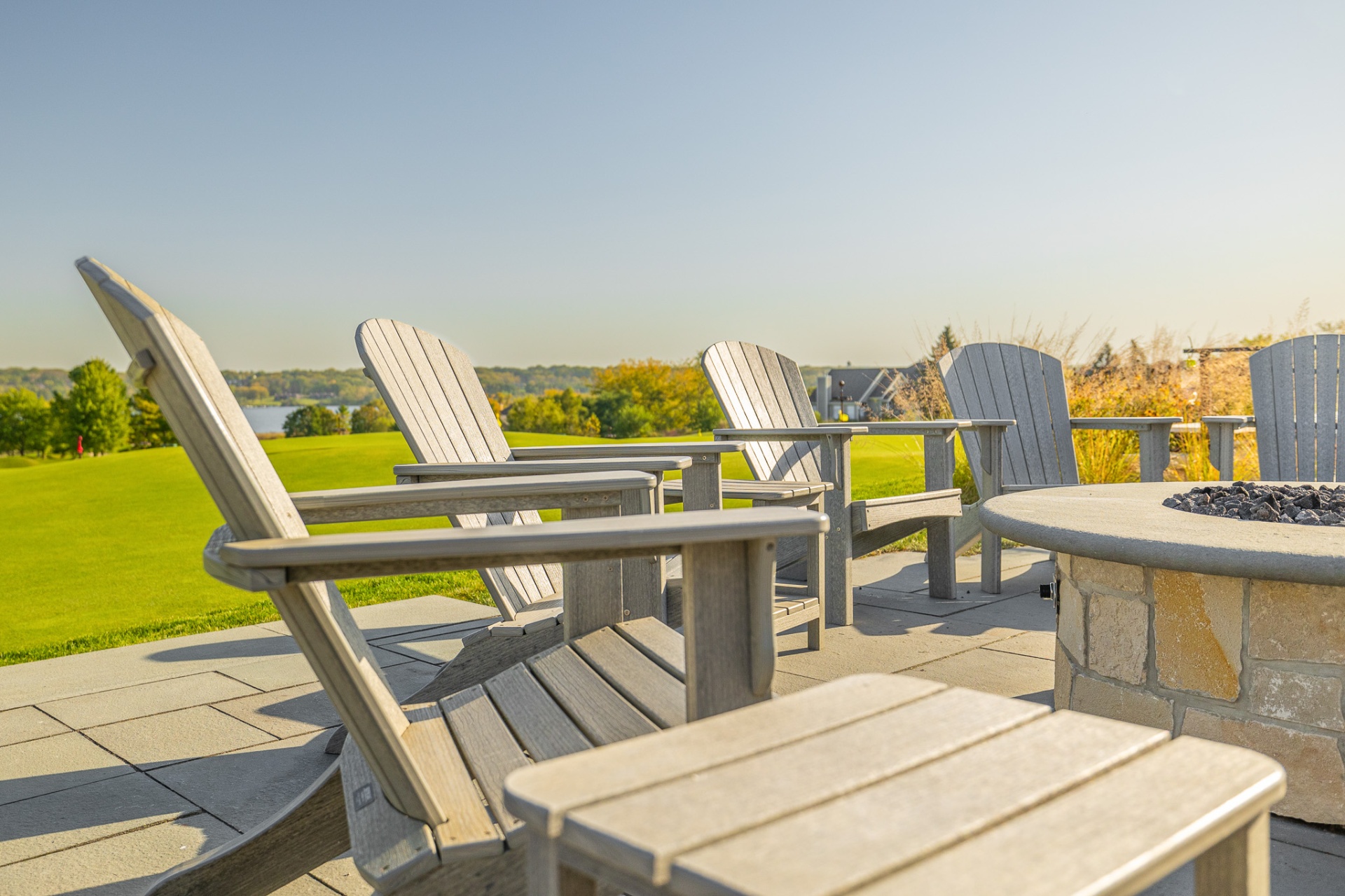 Adirondack chairs around a stone fire pit overlooking the lake at sunset