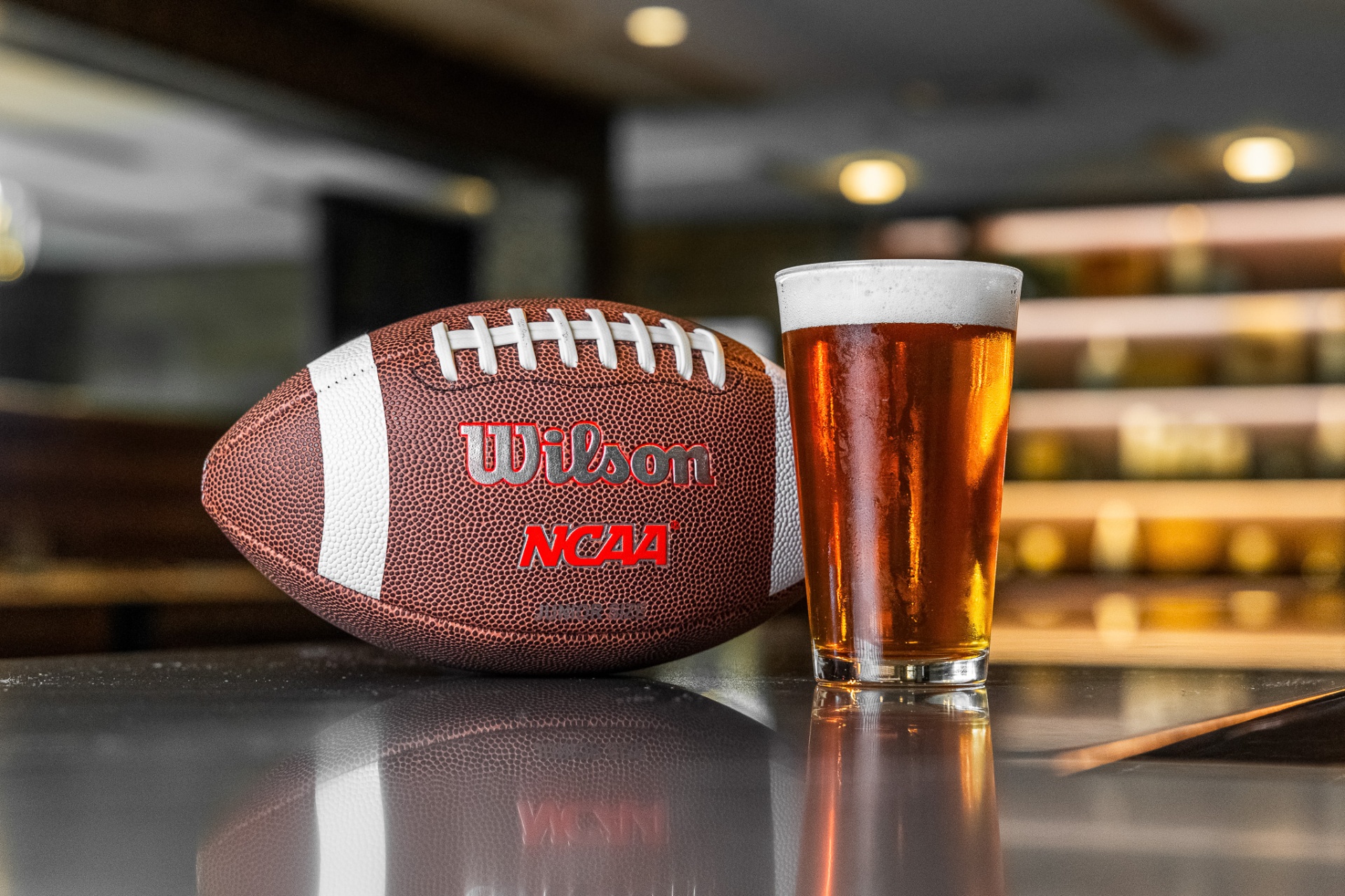 Pint of amber beer next to a Wilson NCAA football on the bar — game day at Mars