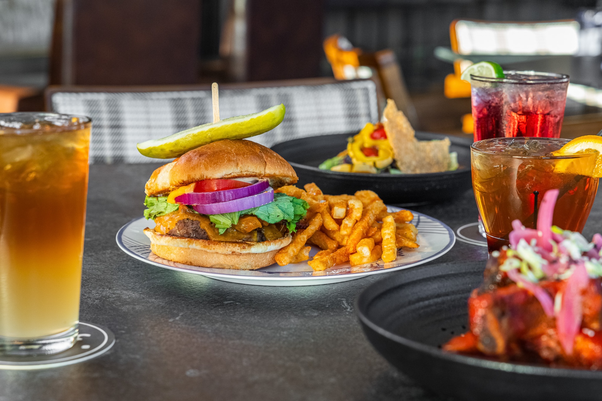 Close-up of a cheeseburger and fries with iced tea and craft cocktails